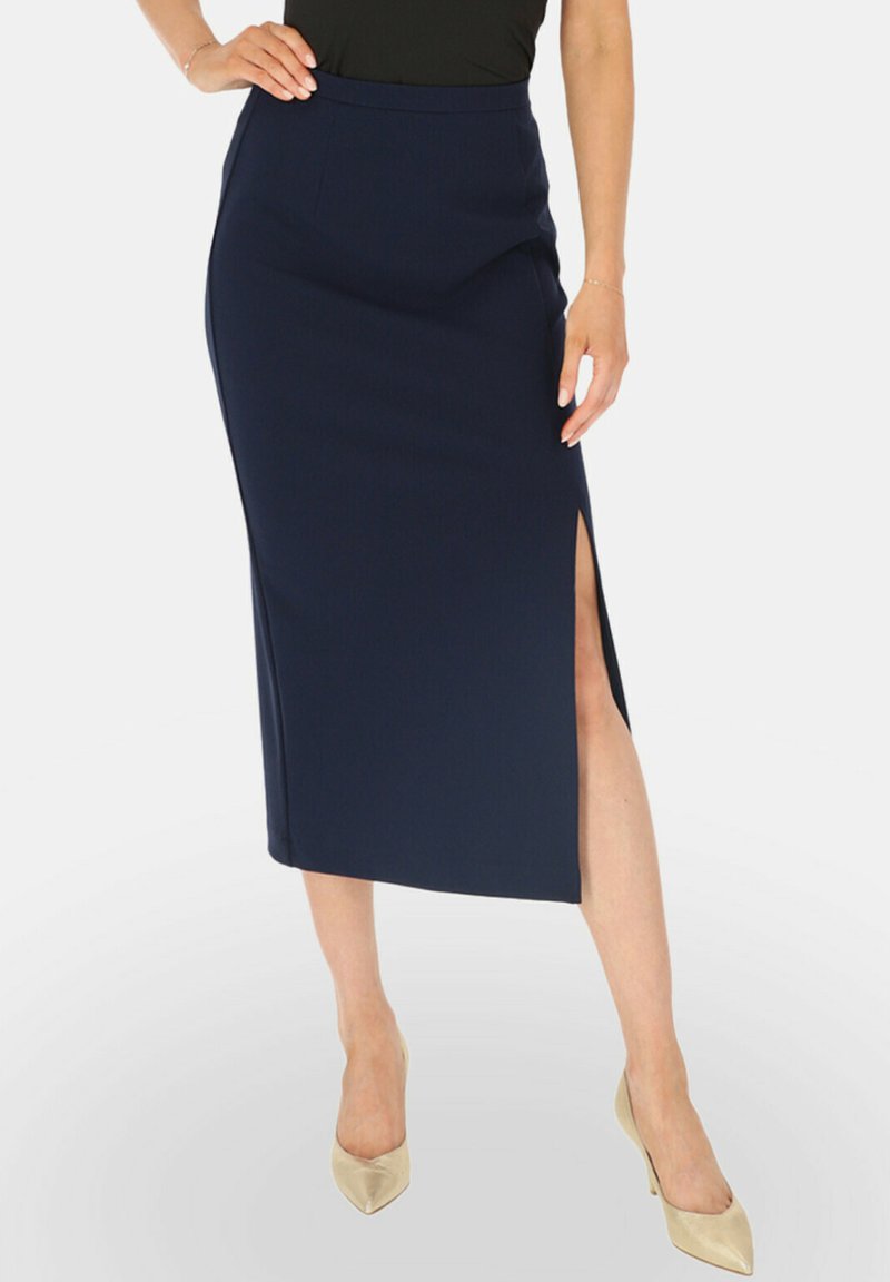 Granatowa, dopasowana spódnica midi z bocznym rozcięciem, uszyta z teksturowanej tkaniny. Po łączona z jasnymi, szpiczastymi szpilkami.