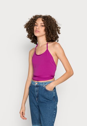 Top halter ajustado em tecido roxo vibrante, combinado com jeans de denim azul de cintura alta com bolsos laterais e um caimento descontraído.