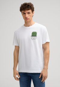 Weißes Baumwoll-T-Shirt mit einer grünen grafischen Illustration von Konservendosen mit Meeresfrüchten auf der Brust. Lässige Passform mit kurzen Ärmeln und einem gerippten Rundhalsausschnitt.