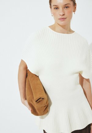 Top blanco de canalé con un dobladillo acampanado combinado con una falda larga marrón. El conjunto se complementa con un bolso de mano marrón y tacones de color claro.