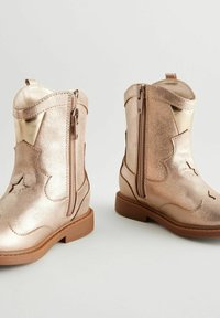 Botas de vaquero infantiles en rosa dorado metálico con cremalleras laterales, un acabado texturizado y detalles de costura decorativa en la parte superior. Suela de goma marrón.