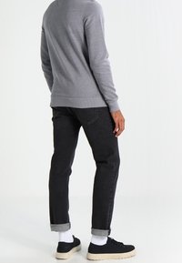 Suéter gris de punto con mangas largas, combinado con jeans negros enrollados en los puños y zapatillas negras con suela color crema.