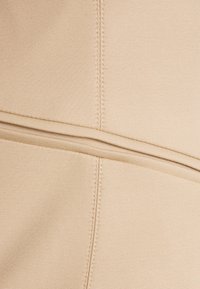 Beżowa tkanina o gładkiej teksturze, z poziomymi liniami ściegów i szwami tworzącymi zorganizowany wzór.