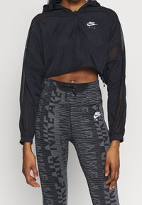 Svart kort jacka med huva och dragkedja, kombinerad med högmidjade leggings med en texturerad, mönstrad design och logotypdetaljer.