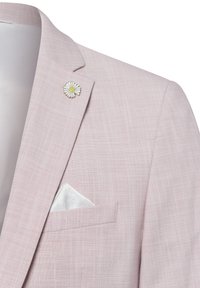 Helles rosa Blazer mit einem strukturierten Gewebe, ausgestattet mit einer weißen Blumenbrosche und einem gemusterten Einstecktuch, das ordentlich in der Brusttasche steckt.