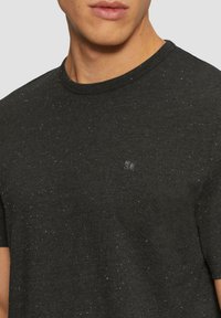 Zwart gespikkeld t-shirt van zachte stof, met een ronde halslijn en een klein logo op de borst. Korte mouwen met een relaxte pasvorm.