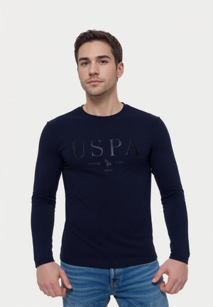 Marineblå langærmet T-shirt i bomuld med et blankt svart "USPA" logo på fronten, rund halsudskæring og tætsiddende design. Bæres med blå jeans.