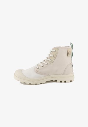 Bottine beige en toile avec embout en caoutchouc, lacets blancs, accents texturés et languette de tirage verte à l'arrière ; semelle extérieure résistante avec crampons.