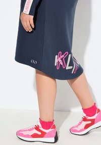 Abito felpa navy con accenti grafici rosa e bianchi, abbinato a sneakers chunky rosa e rosse e calze rosa a costine. Tessuto morbido.
