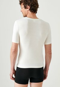 Witte kortemouwen shirt gemaakt van zachte stof, aansluitende pasvorm, ronde halslijn, getoond vanaf de achterkant met zwarte aansluitende shorts. Minimalistisch ontwerp.