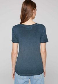 Tmavě modré tričko s krátkým rukávem, kulatým výstřihem a jemnou texturou. Na zadní straně u límce má decentní logo "SOCCX".