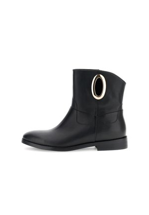 Stivale alla caviglia in pelle nera con punta arrotondata, texture liscia e un distintivo accent gold ovale sul lato. Suola piatta.