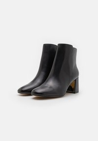 Botines de cuero negro con una textura suave, punta afilada y tacón cuadrado que presenta un acento metálico en la parte trasera.