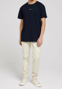 Granatowy bawełniany t-shirt z nadrukiem tekstowym na piersi, zestawiony z jasnobeżowymi spodniami i beżowymi sneakersami; luźny krój i krótkie rękawy.