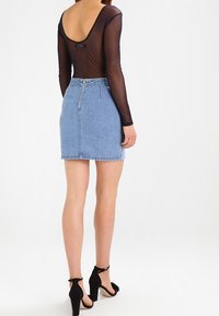 Schwarzes, transparentes Langarmoberteil mit tiefem Rückenausschnitt, kombiniert mit einem hellblauen Jeans-Minirock mit Reißverschluss und fransigem Saum. Schwarze High-Heels.