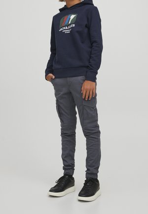 Marineblauwe hoodie met logo-afbeelding, grijze cargobroek met zakken en zwarte sneakers met witte zolen. Casual streetwear stijl.