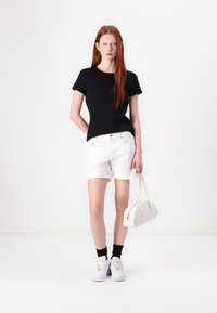T-shirt nera a maniche corte, pantaloncini in denim bianchi, sneakers bianche e una borsa leggera color beige. Design semplice con una vestibilità casual e linee pulite.