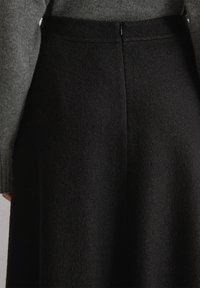 Achteraanzicht van een persoon die een hoog-waist zwarte rok met een centrale rits en een grijze gebreide trui draagt.