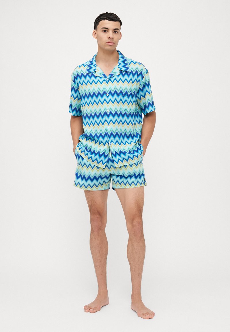Set di maglietta a maniche corte e pantaloni corti con motivo a zigzag, caratterizzato da tonalità blu e verde, tessuto leggero e una vestibilità rilassata.