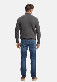 Suéter de punto gris con cuello alto, combinado con jeans de mezclilla azules y zapatillas color marrón claro. La textura es suave y ajustada.
