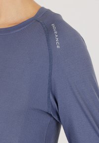 Langärmliges Sportoberteil aus glattem, elastischem Material in Blau, mit geripptem Muster an den Schultern und "ENDURANCE" Branding.
