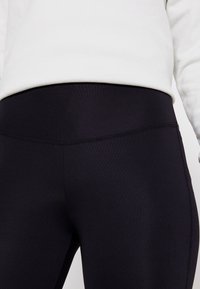 Leggings negros hechos de un tejido elástico, con un diseño de cintura alta y costuras planas para mayor comodidad. Vista en primer plano con detalles de textura mínimos.