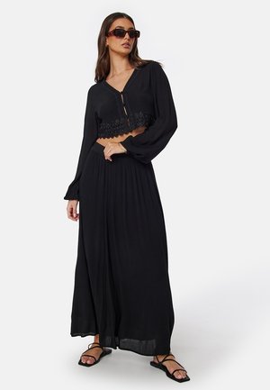 Completo nero in due pezzi composto da un top corto con pizzo e una lunga gonna plissettata. Il tessuto sembra leggero con una finitura liscia.