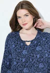 Blouse floral bleu marine à manches longues, avec un décolleté en forme de trou de serrure et de délicats motifs floraux bleu clair sur l'ensemble. Tissu au toucher lisse.