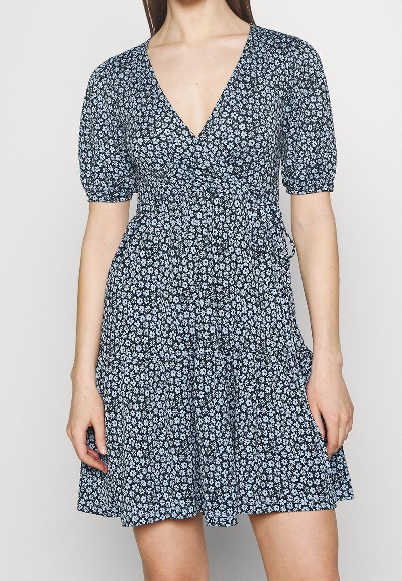 Černé zavinovací šaty s květinovým vzorem v světle modré barvě, s krátkými puffovými rukávy a volánkovým lemem sukně. Vyrobené z lehkého materiálu.