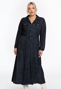 Robe en denim foncé avec des manches longues, un col, deux poches poitrine et une taille ceinturée. Présente une fermeture à boutons et un design fluide jusqu'aux chevilles.