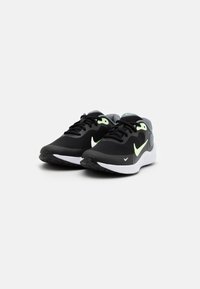 Baskets de sport noires avec une tige en mesh texturé, une semelle blanche et des accents vert fluo sur les lacets et le logo Nike. Conception légère.