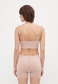 Naken ribbad bralette med tunna band som kombineras med matchande högmidjade shorts, båda tillverkade av mjukt, stretchy tyg.
