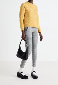 Gul strukturerad tröja, grå rutiga byxor, svart handväska, vita strumpor och kraftiga svarta skor med spänne.