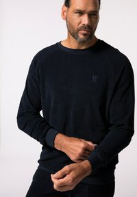 Sudadera de forro polar azul marino con cuello redondo, puños acanalados y un logotipo sutil en el pecho, que presenta una textura suave y un corte relajado.