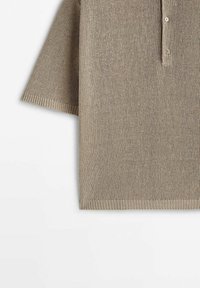 Beige knit polo shirt with short sleeves, multiple buttons at the collar, and ribbed edges, featuring a textured fabric design.