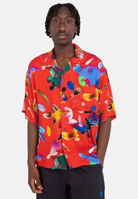 Red short-sleeve shirt featuring an abstract pattern in various colors. Made of smooth fabric with a button-down front and pocket.