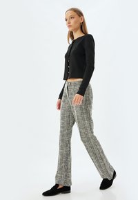 Svart ribbad cardigan med knappar, parat med högmidjade, strukturerade svartvita randiga byxor och svarta slip-on skor.