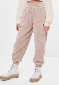 Lichtbruine, vlezige fleece joggers met een hoge tailleband, zijzakken en geribbelde enkelmanchetten, gecombineerd met stevige witte laarzen.