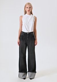 Witte mouwloze top gecombineerd met high-waisted, wijde zwarte jeans met opgevouwen, lichtgrijze mouwen en subtiele zakken.