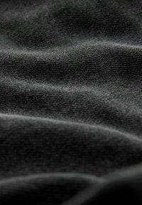 Tessuto nero con una superficie texture, che mostra morbide pieghe e grinze. Il materiale appare liscio, con delicati motivi a maglia visibili in tutto il tessuto.