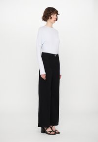Pantaloni neri a vita alta e a gamba larga con tasche frontali, abbinati a un top fitted bianco a maniche lunghe, con scollatura rotonda e una leggera texture.