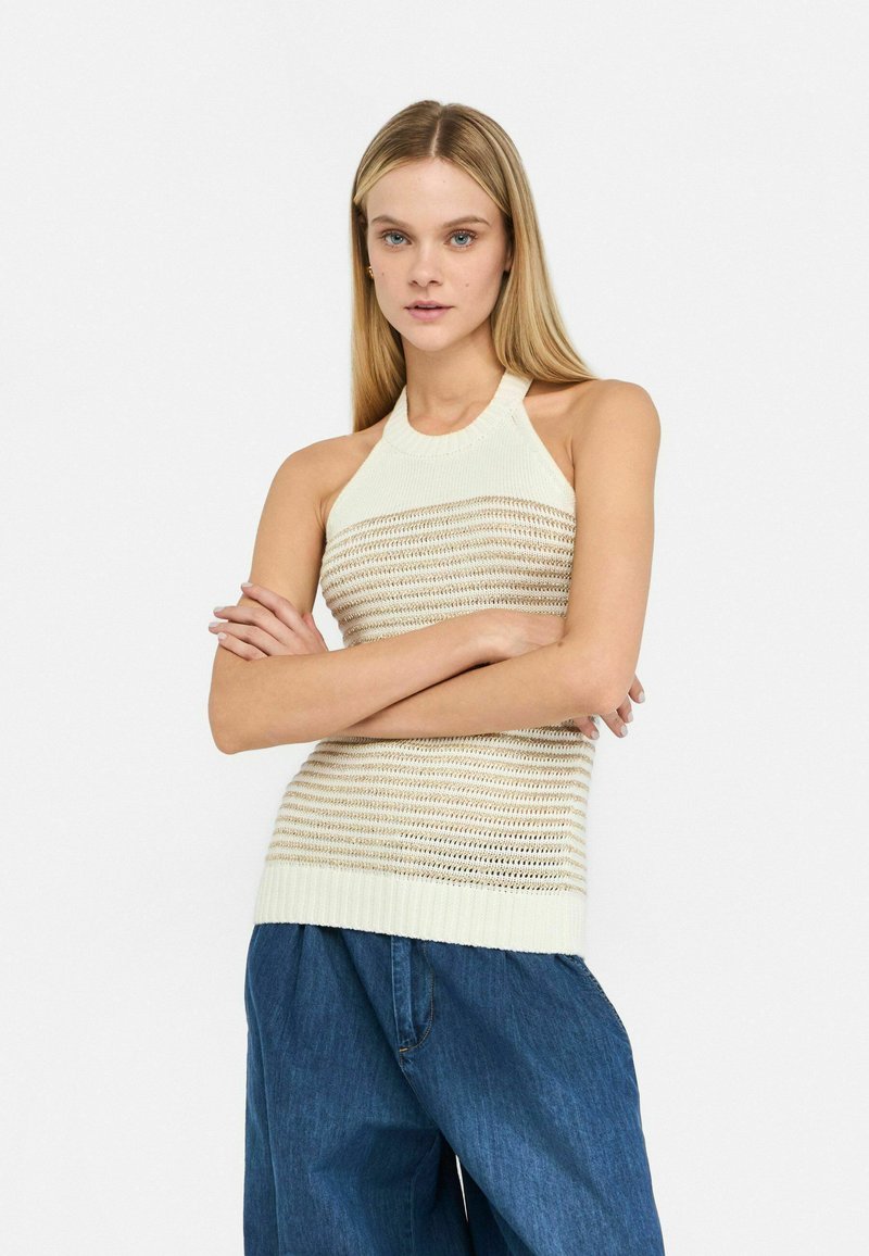 Top in maglia crema con un design a collo halter e un motivo a righe ad uncinetto, abbinato a pantaloni in denim blu larghi. Texture liscia, finitura morbida.