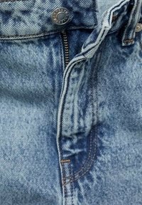 Denim hlače svetlo modre barve z blagim teksturnim učinkom. Imajo kovinski gumb, zadrgo in kontrastno oranžno šivanje. Poglejmo bližje pas.