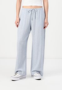 Pantalons larges bleu clair avec des rayures blanches verticales, confectionnés dans un tissu doux, dotés d'une taille élastique et d'un cordon de serrage.