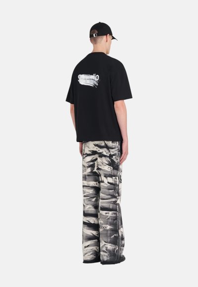 T-shirt noir surdimensionné avec un graphique blanc au dos, associé à un pantalon large avec un motif abstrait noir et blanc.