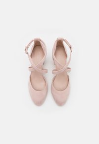 Chaussures roses en suède à talons bas, bouts ronds et brides croisées à la cheville. Intérieur lisse et design minimaliste.