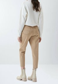 Pantalones cortos beige con bolsillos traseros, combinados con botines beige. La parte superior es un suéter blanco texturizado con un corte relajado.