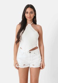 Witte gebreide haltertop met een ruitpatroon en een centrale knoop, gecombineerd met beschadigde witte denim shorts met rafelige randen.