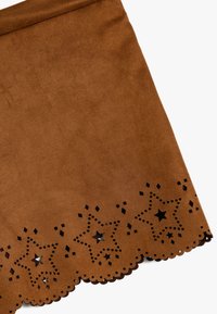 Brun ruskindnederdel med bølget kant, der har udskårne stjerner og diamantmønstre. Glat tekstur med en strømlinet silhuet.