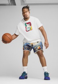 Tricou alb cu un imprimeu colorat, şorturi cu un model ce prezintă mingi de baschet pe un fundal învârtitor şi pantofi sport multicolori.